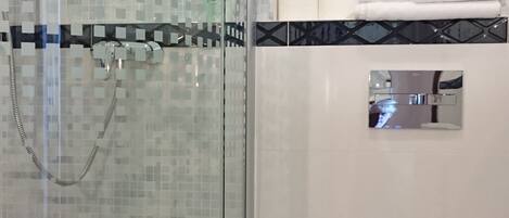 Un baño moderno con ducha acristalada, inodoro y estante con artículos de aseo.