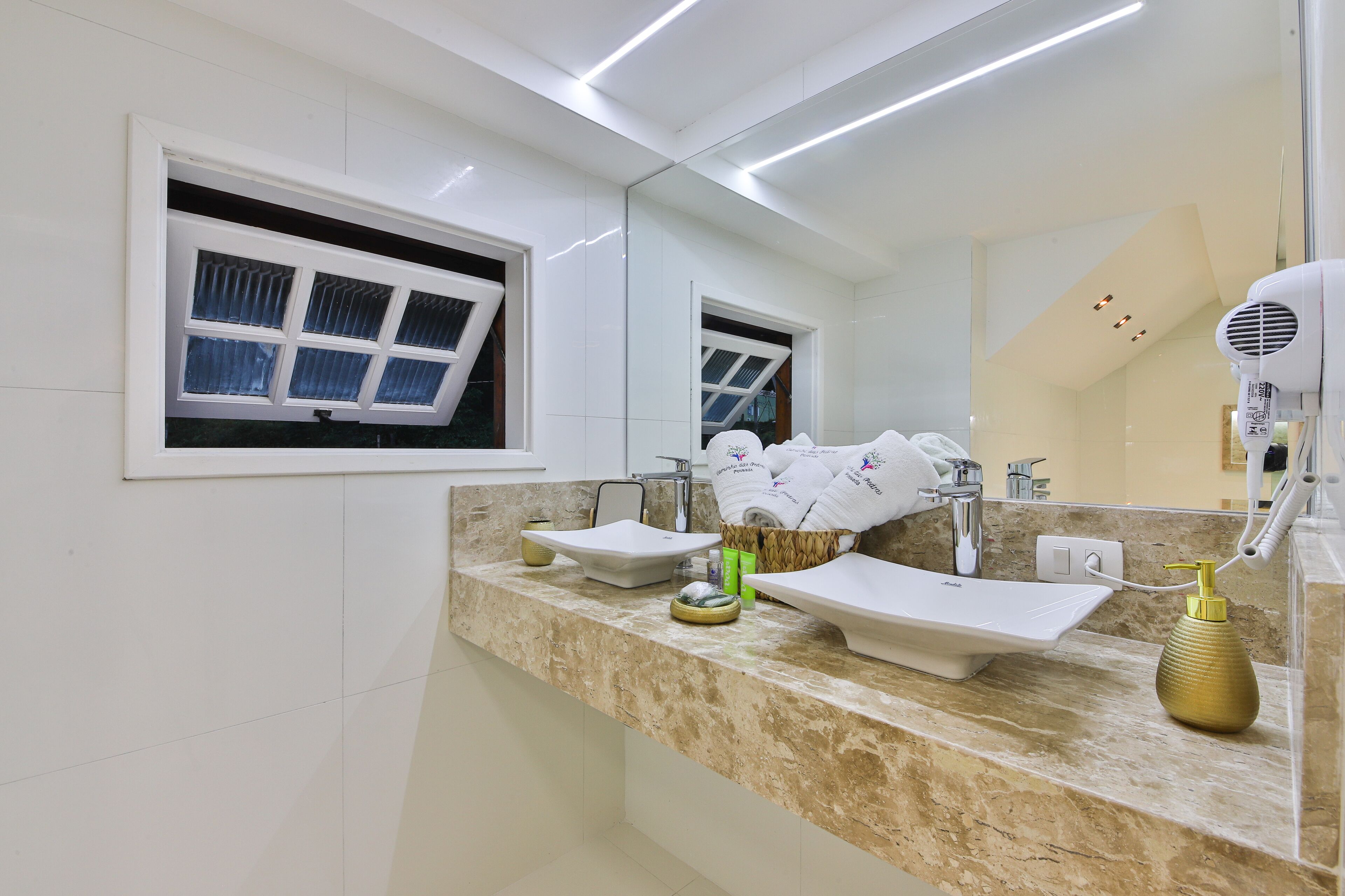 A modern bathroom with a large mirror, a sink, a window with blinds, and a hairdryer on the counter.