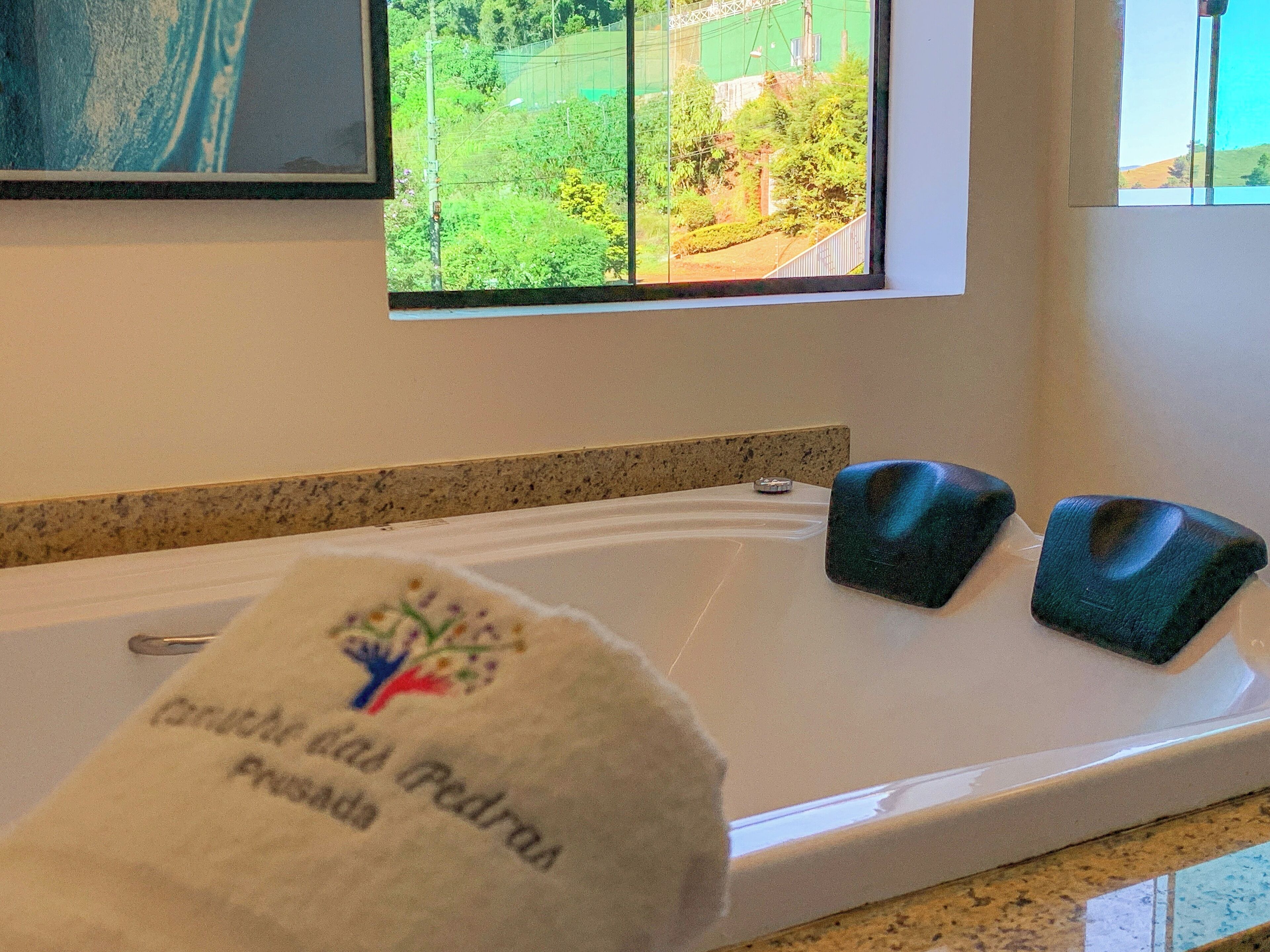 A bathroom with a bathtub, a towel with a logo, and a window with a view of greenery.
