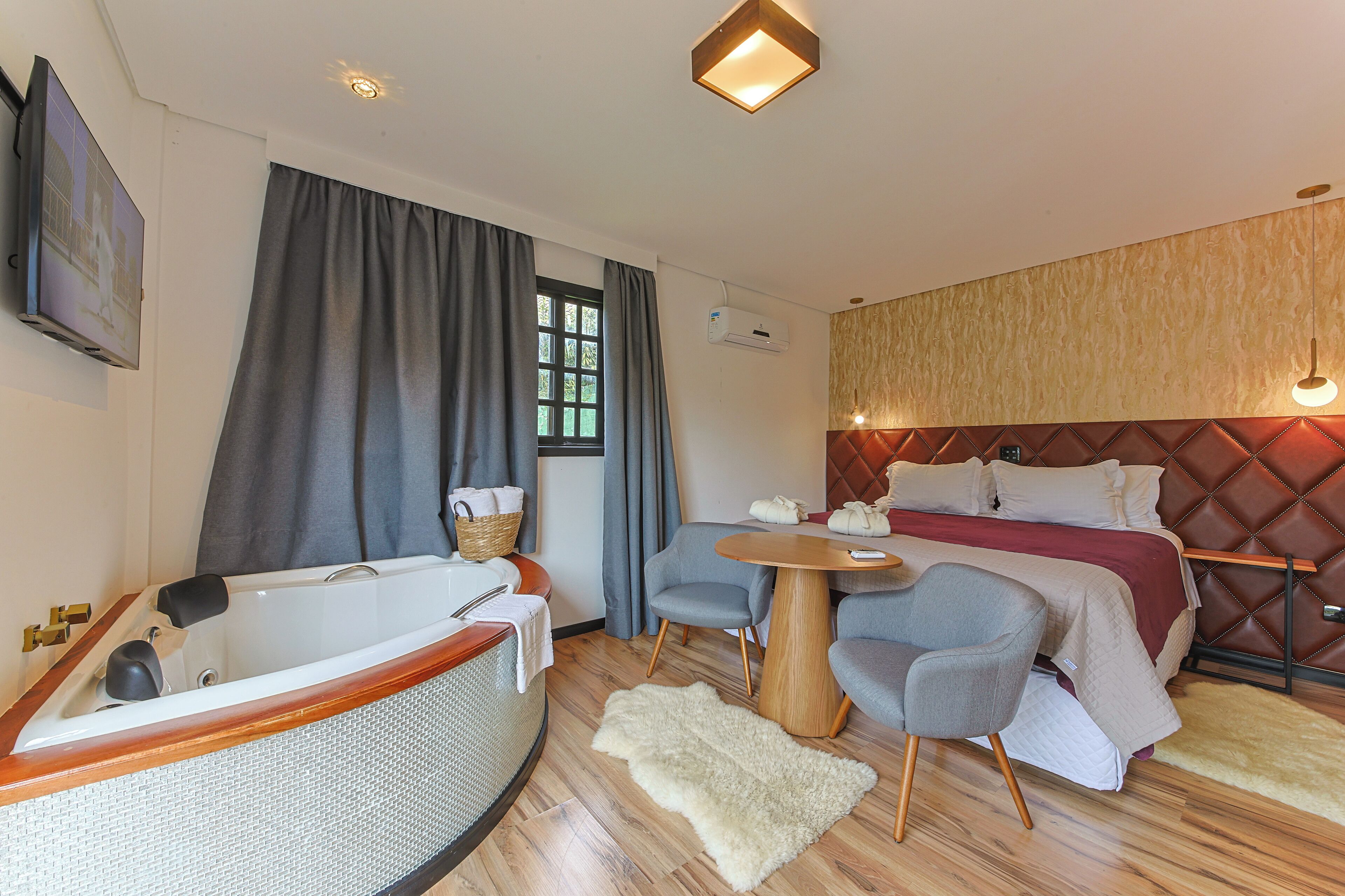 Habitación de hotel moderna con una bañera grande, una cama cómoda, una mesita redonda pequeña y una zona de estar con sillas.