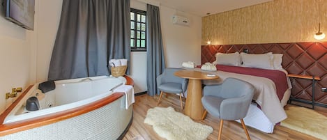 Habitación de hotel moderna con una bañera grande, una cama cómoda, una mesita redonda pequeña y una zona de estar con sillas.