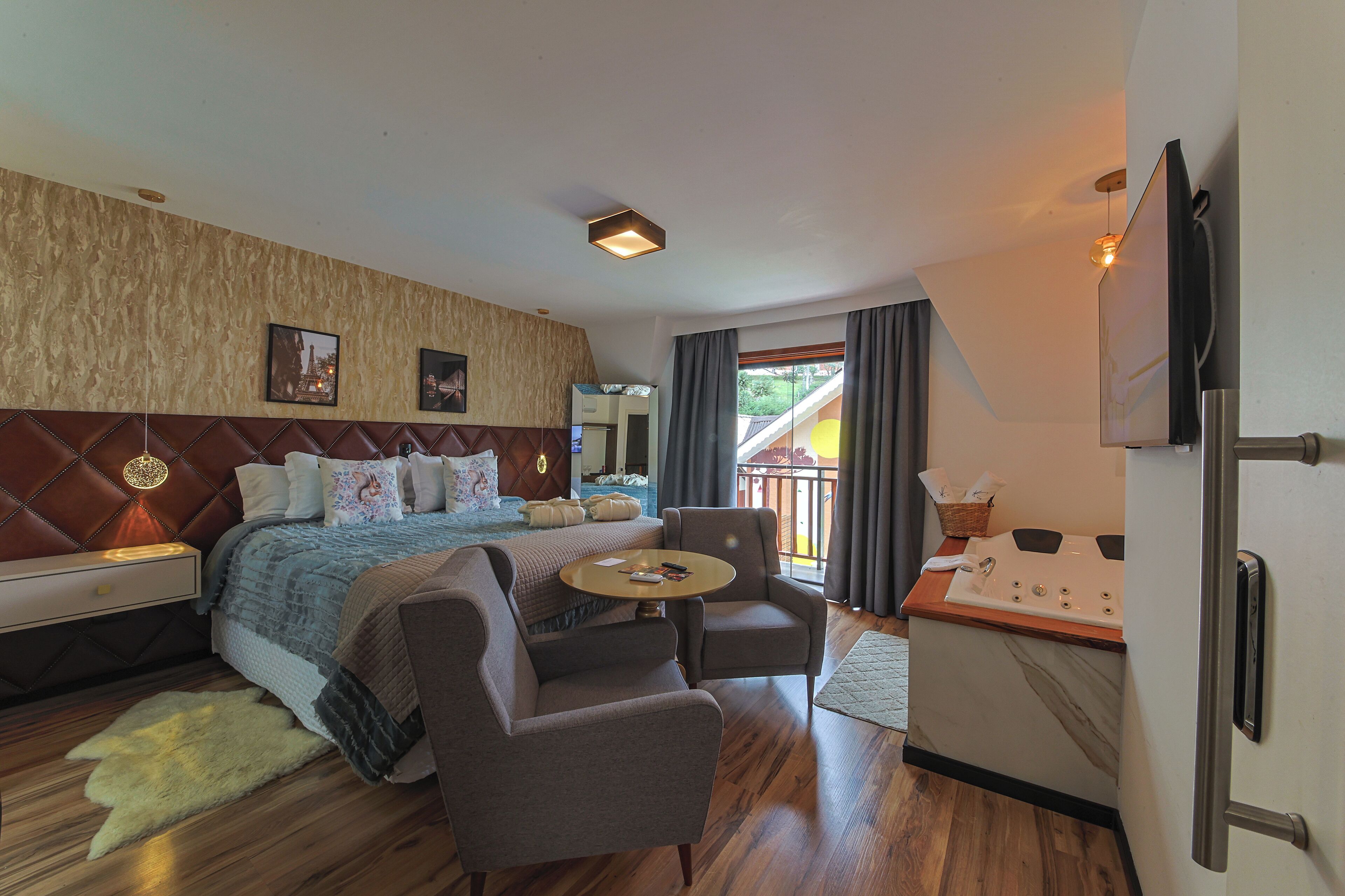A hotel room with a bed, a sofa, a small table, a TV, and a bathroom with a sink and mirror.