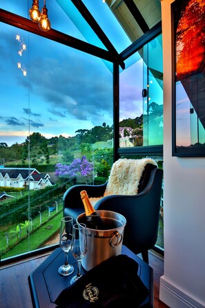 A room with a large window, a chair, a bottle of champagne, and two glasses on a tray.