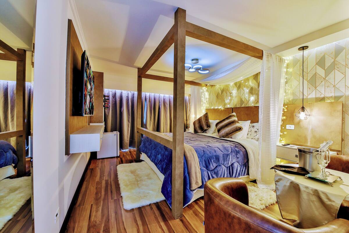 Een slaapkamer met een houten plafond, een bed met een blauwe dekbedovertrek, een witte vloerkleed en een houten stoel.