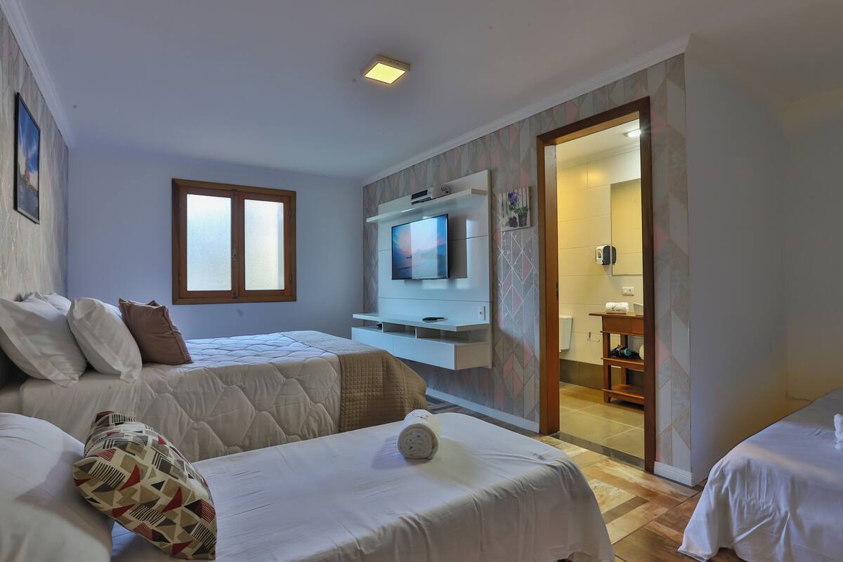 Een hotelkamer met twee bedden, een televisie, een kleine badkamer en een raam.