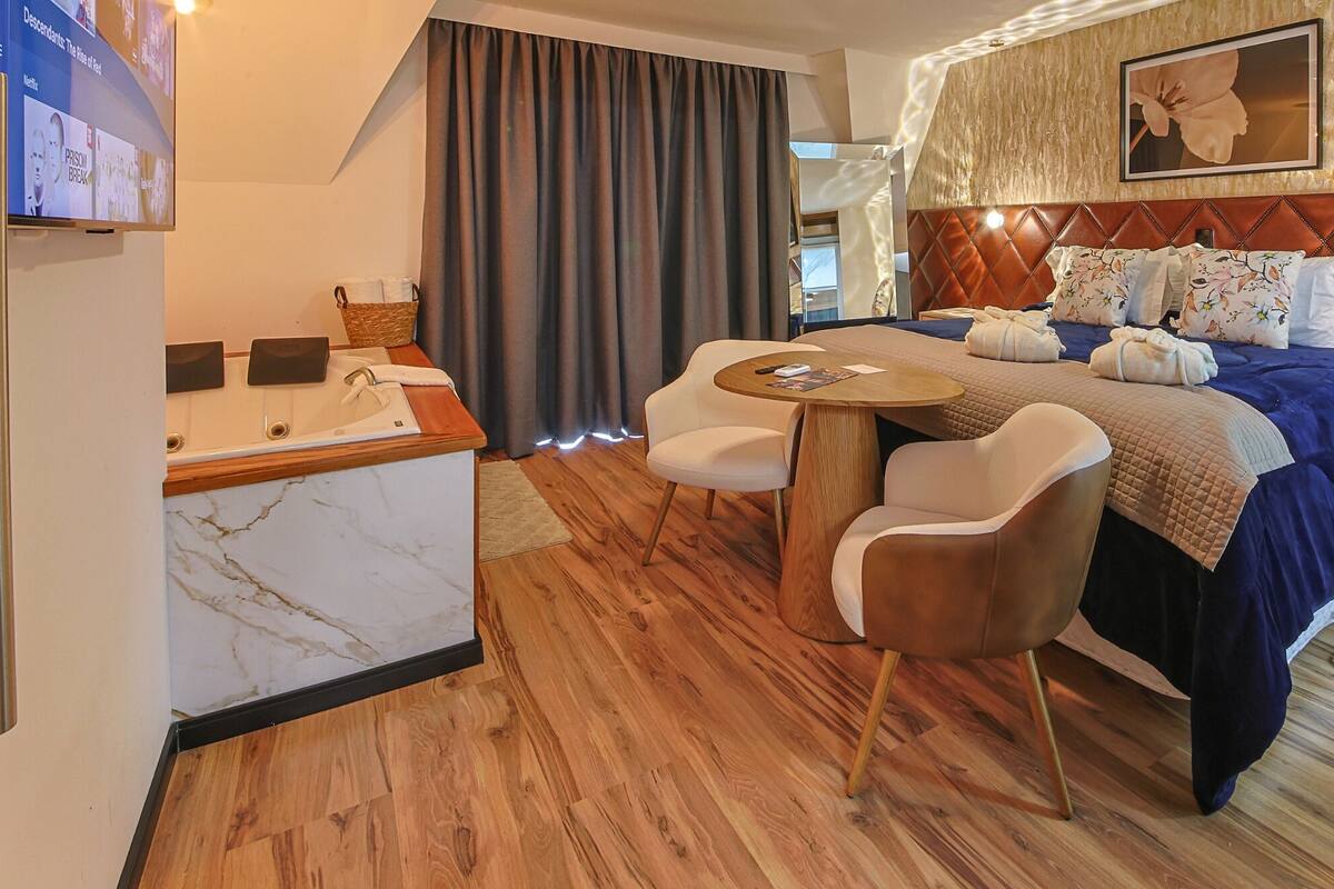 Een hotelkamer met een bed, een bureau met een wastafel, twee stoelen en een televisie waarop een menu staat.