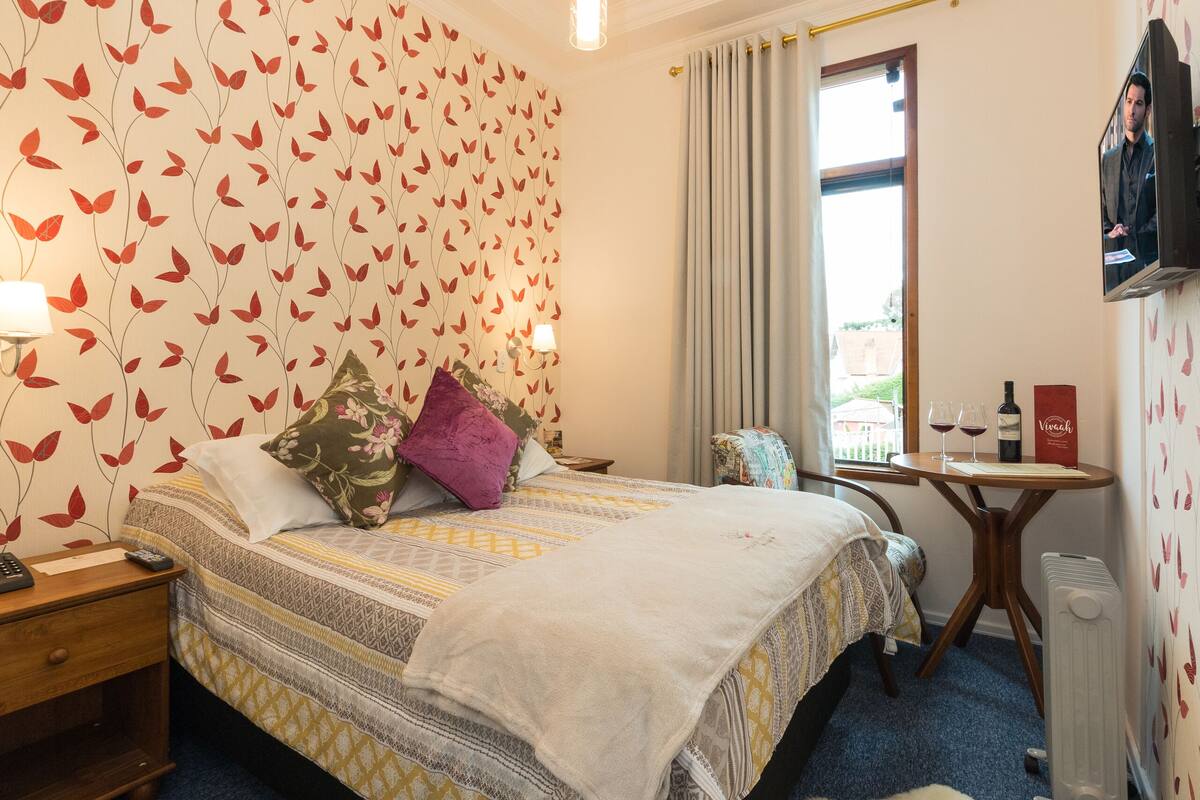Een hotelkamer met een bed, een bureau, een televisie en een raam met gordijnen.