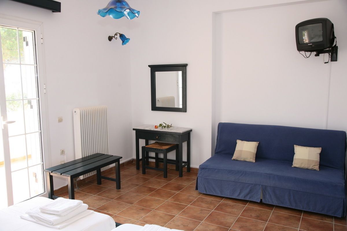 A room with a bed, a bench, a table with a mirror, a blue sofa, and a television mounted on the wall.