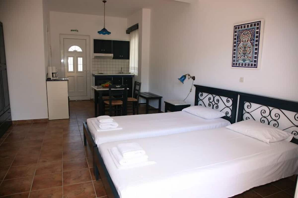 A hotel room with two beds, a small kitchenette, a dining area, and a bathroom.