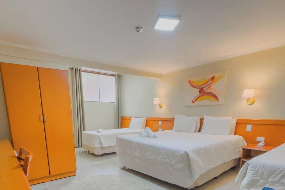 Una habitación de hotel con dos camas, un armario, un escritorio y una ventana.