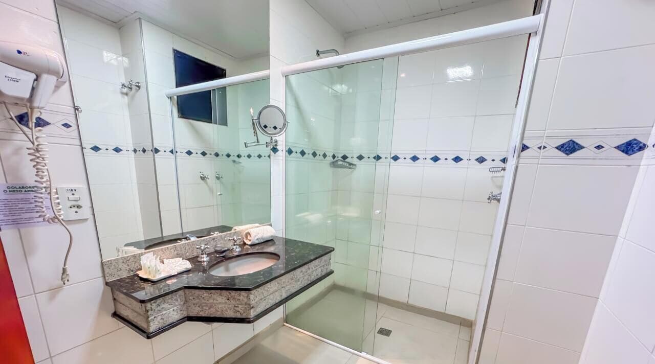 Een moderne badkamer met een douchecabine van glas, een wastafel met granieten blad en een spiegel.