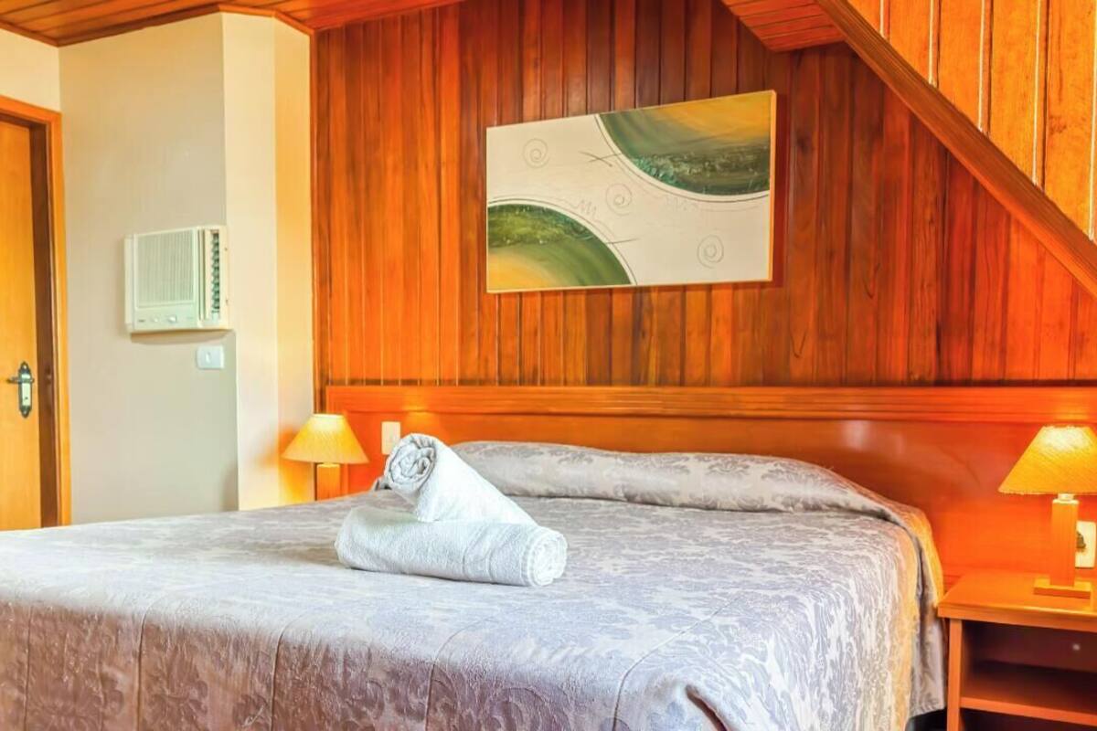 Una habitación de hotel con techo de paneles de madera, una cama con toalla enrollada, dos lámparas de noche y aire acondicionado de pared.