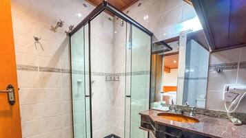 A modern bathroom with a glass shower enclosure, a sink with a marble countertop, and a mirror with a towel dispenser.
