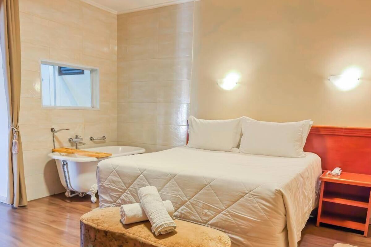 Habitación de hotel con cama, baño con bañera y una mesita con teléfono.
