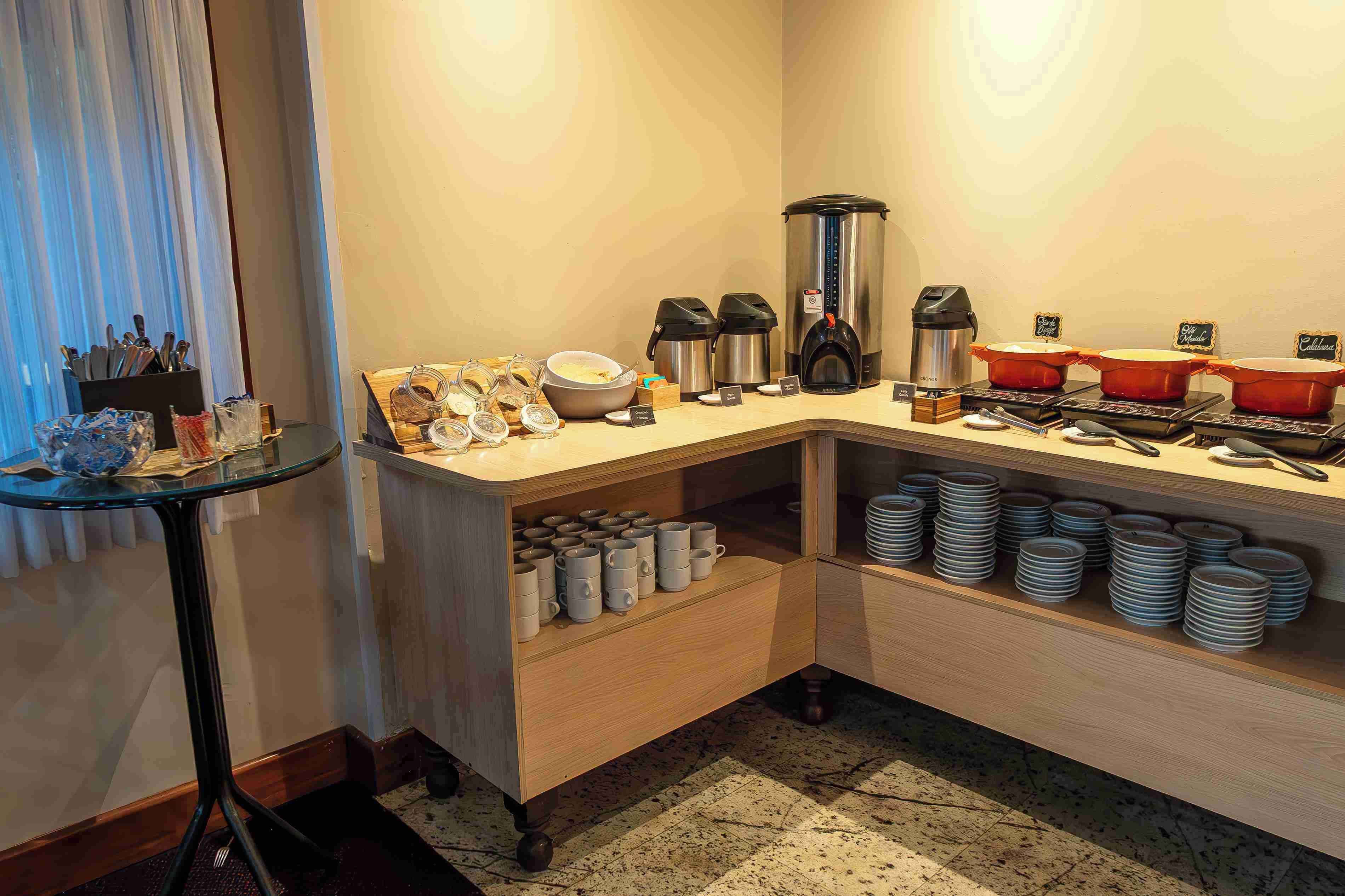 Una barra de desayuno con cafeteras, un hervidor y una variedad de tazas y platos.