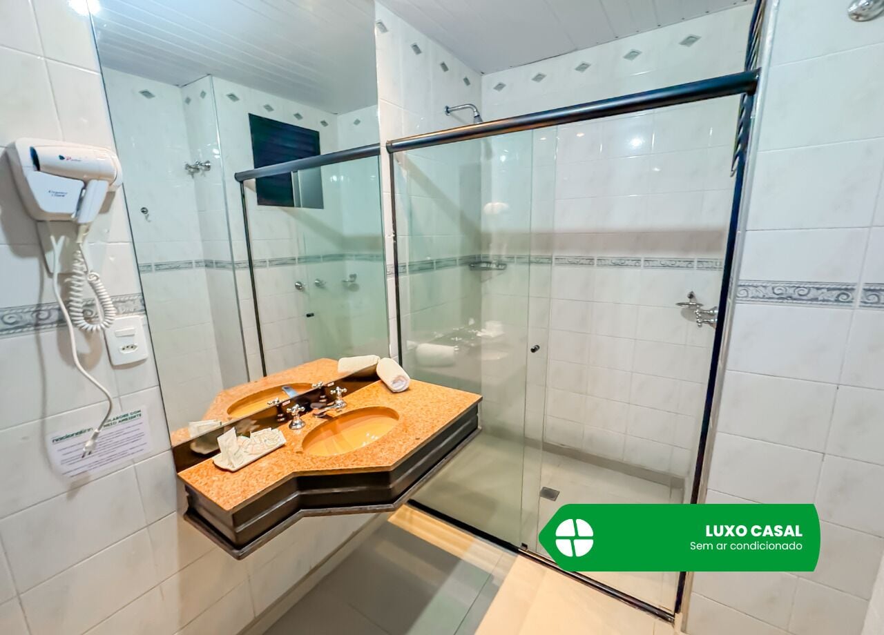 A bathroom with a glass-enclosed shower, a sink with a towel, and a hairdryer on the wall.