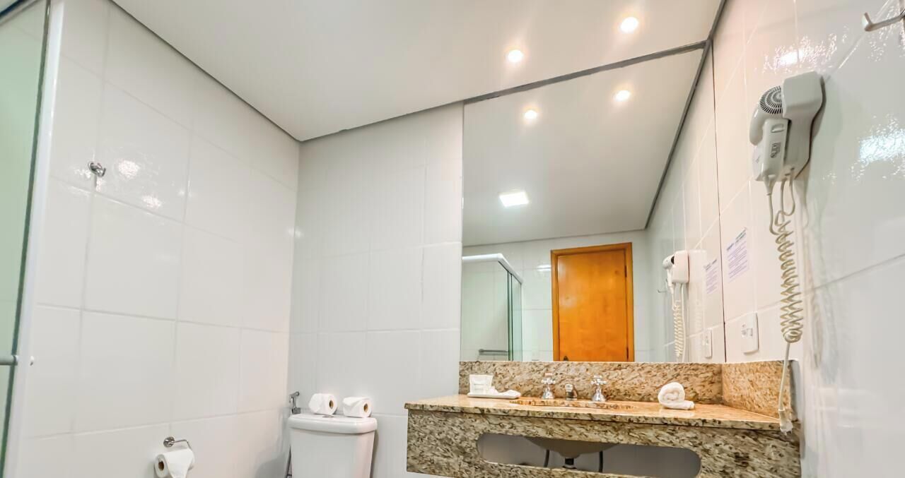 Une salle de bain moderne avec des carreaux blancs, un comptoir en granit, un sèche-cheveux et un miroir.