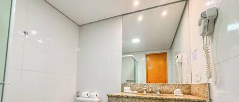 A modern bathroom with white tiles, a granite countertop, a hairdryer, and a mirror.