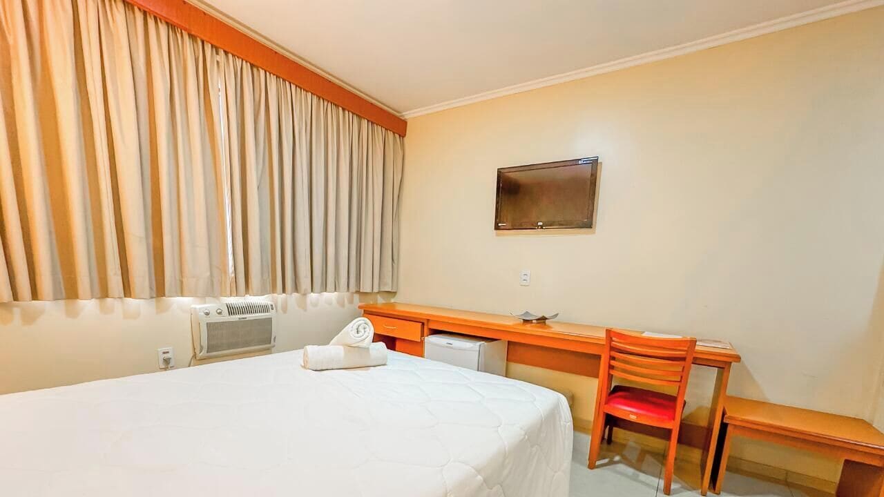 A hotel room with a bed, a desk, a chair, a television, and a window with curtains.