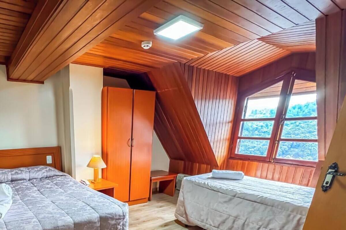 Un dormitorio con dos camas, un armario, una mesita de noche con lámpara y una ventana con vistas a árboles.