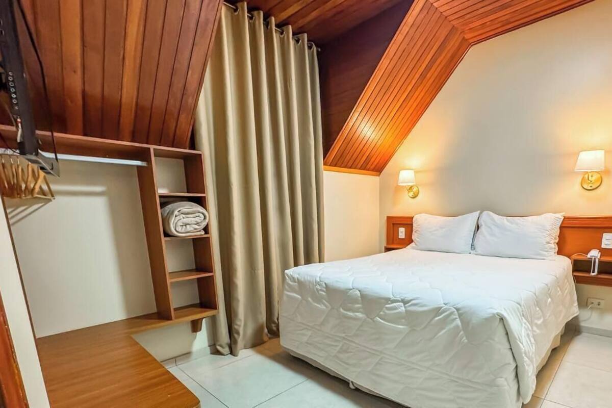 Un dormitorio con cama, cabecero de madera, dos lámparas fijadas a la pared, un armario y techo con vigas de madera.