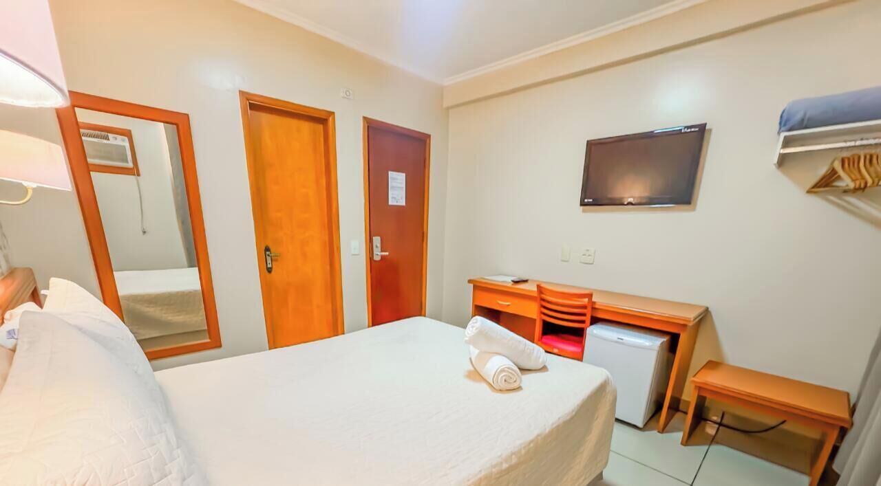 A hotel room with a bed, a desk, a television, and a mirror.