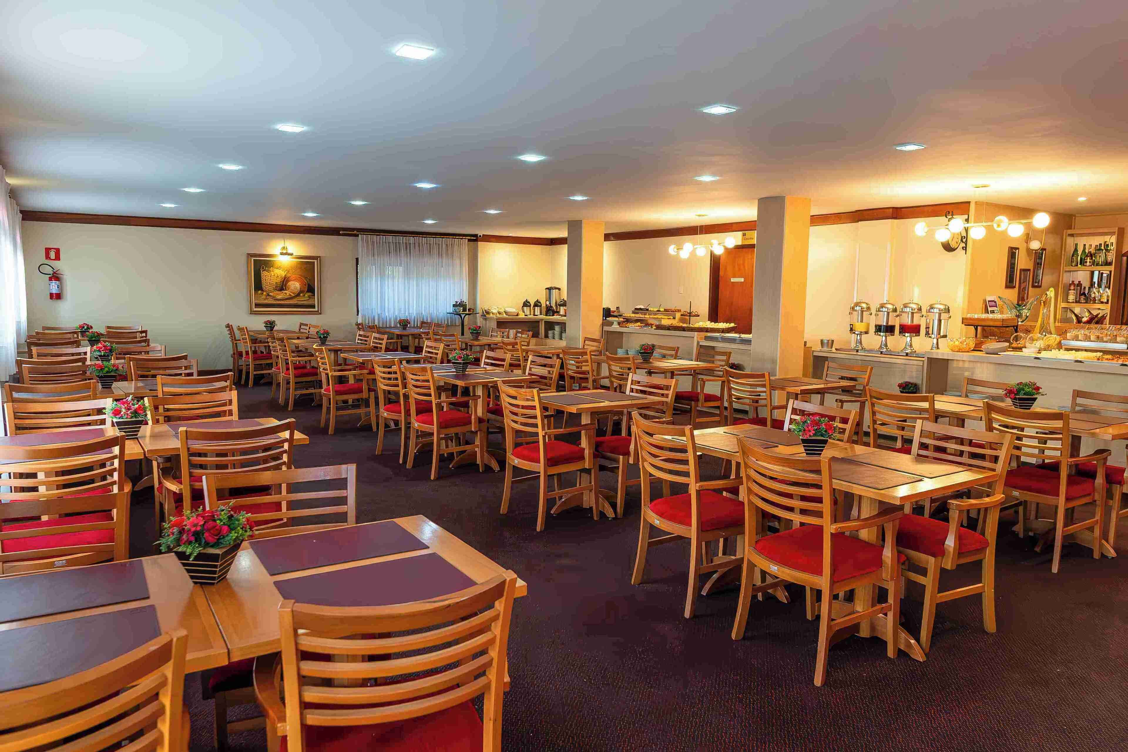 Un restaurante amplio con varias mesas y sillas de madera, una zona de bar y un extintor en la pared.