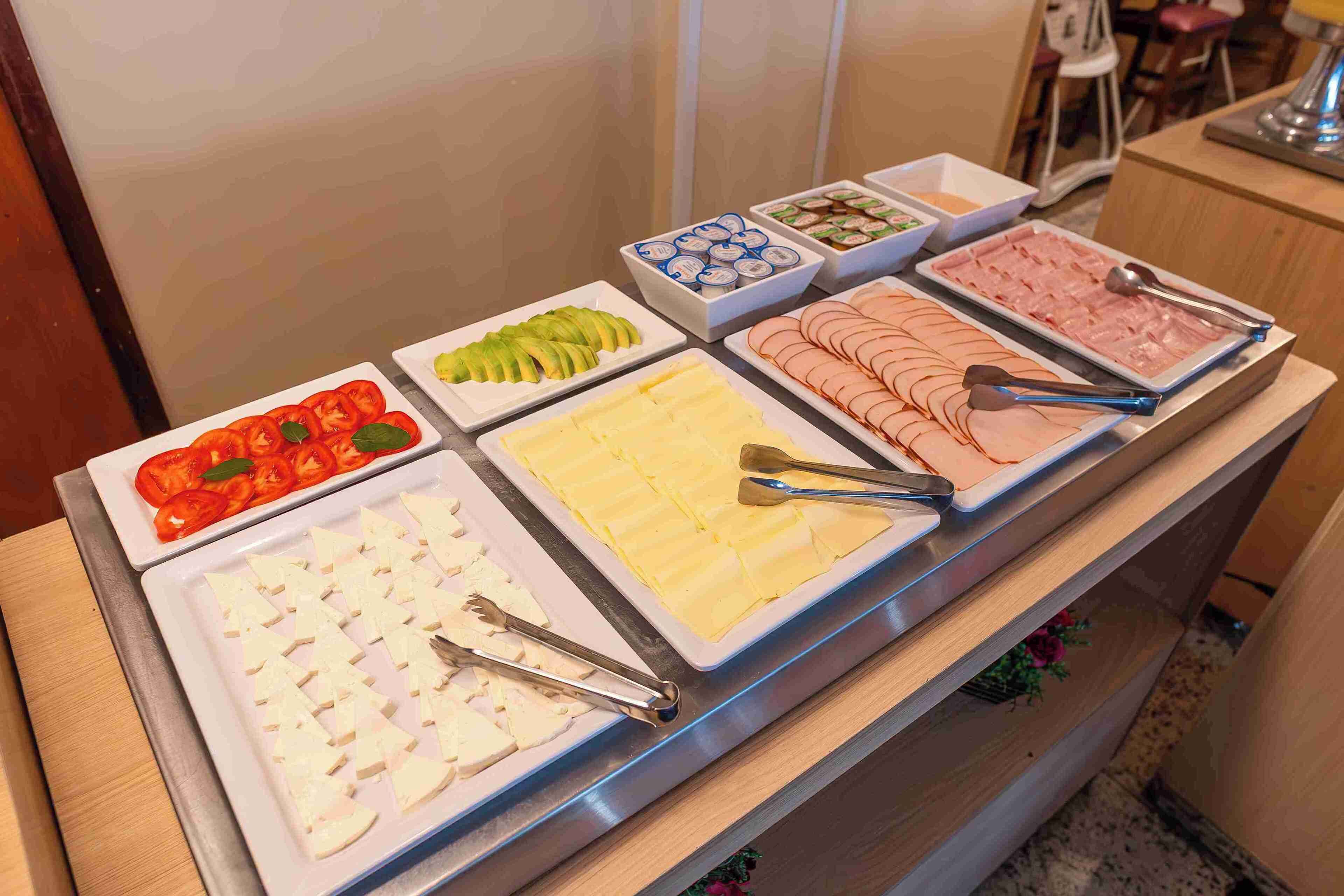 Buffet-pöydässä on tarjolla monenlaista ruokaa, kuten viipaloituja tomaatteja, juustoa ja lihaa.