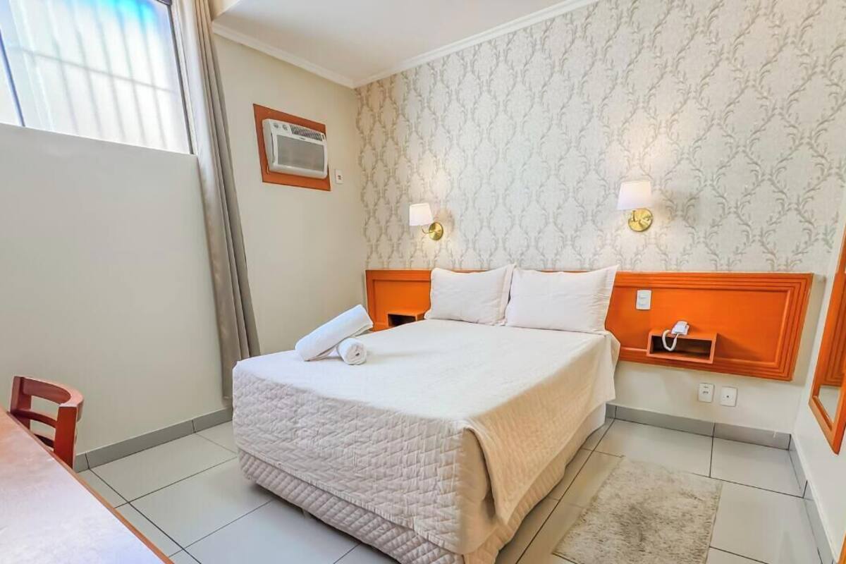 Habitación de hotel con cama, mesitas de noche, un espejo y una ventana con persianas.