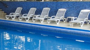 Una piscina con pared de azulejos azules y sillas reclinables blancas.