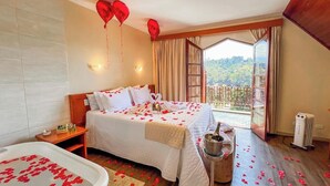 Habitación de hotel con cama, bañera con pétalos de rosa, balcón con vistas y calefacción en el suelo.