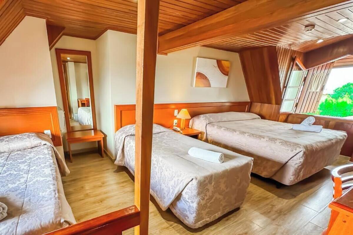 Una habitación con dos camas, vigas de madera en el techo, un espejo y ventana con vistas a la vegetación.