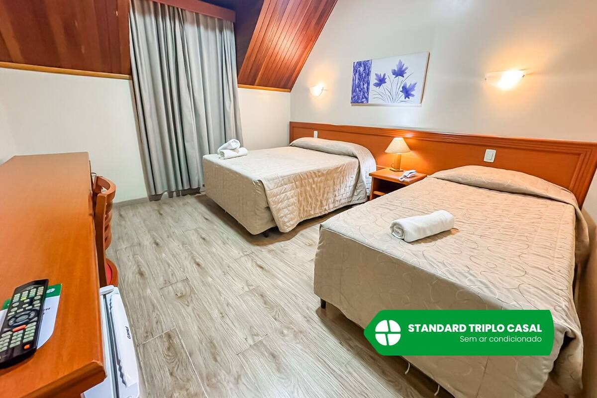 Habitación estándar triple con dos camas individuales, un escritorio de madera, una lámpara y un cuadro en la pared.