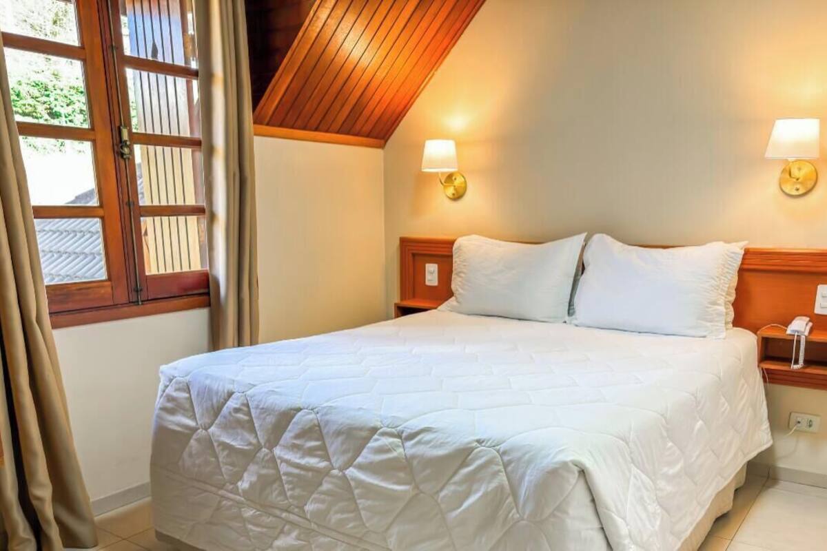 Una cama bien hecha con un edredón blanco acolchado, cabecera de madera y lámparas de noche.