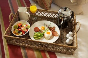 Una bandeja de desayuno con huevos, aguacate y tocino, un tazón de fruta, un vaso de jugo de naranja, una cafetera y saleros y pimenteros.
