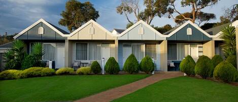 A row of three-story mobile homes with a central driveway, surrounded by well-maintained lawns and small trees.