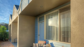 Un patio con una mesa redonda y sillas, una planta en maceta y una ventana con cortinas.