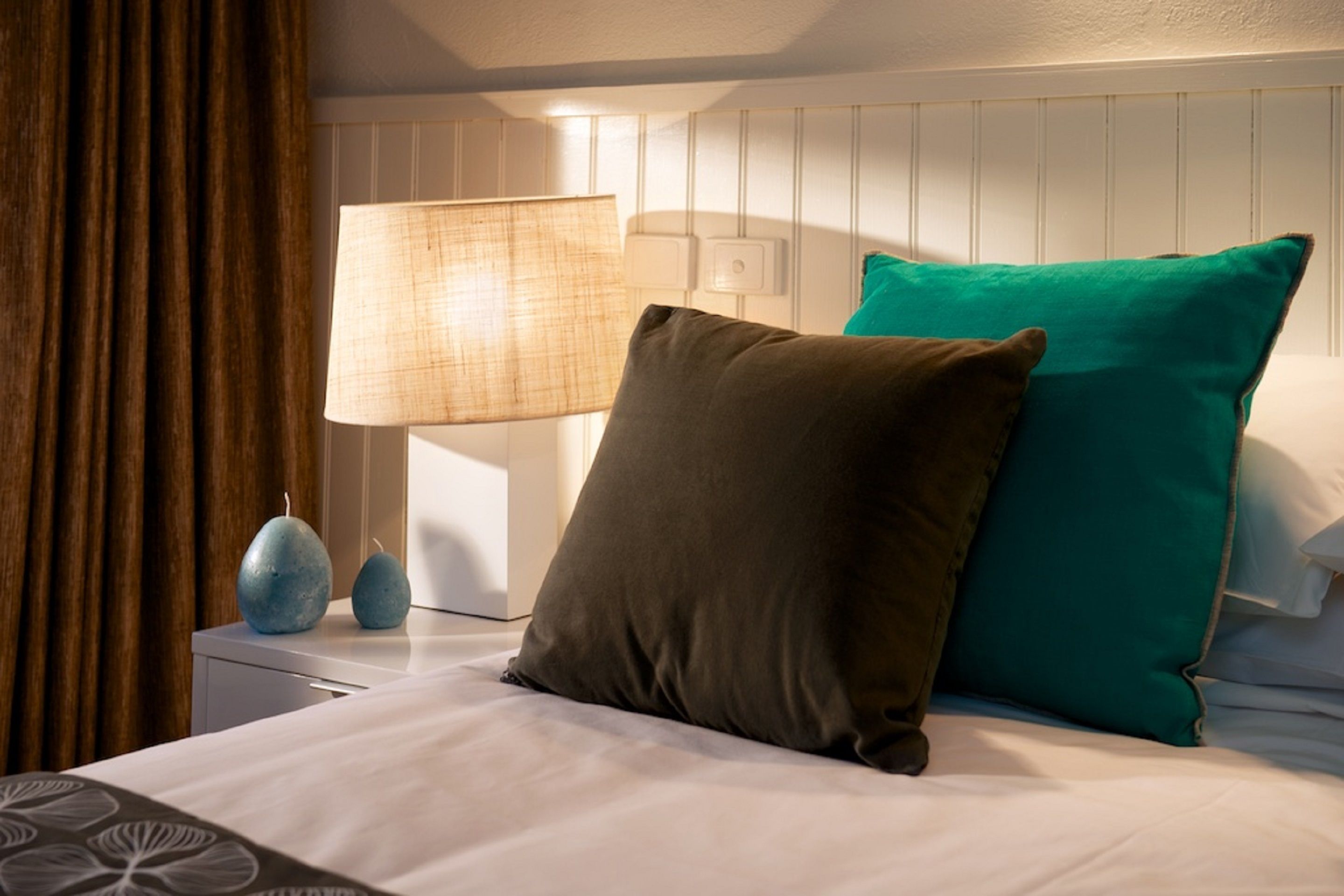 A neatly made bed with two pillows, a lamp, and a vase on a bedside table.
