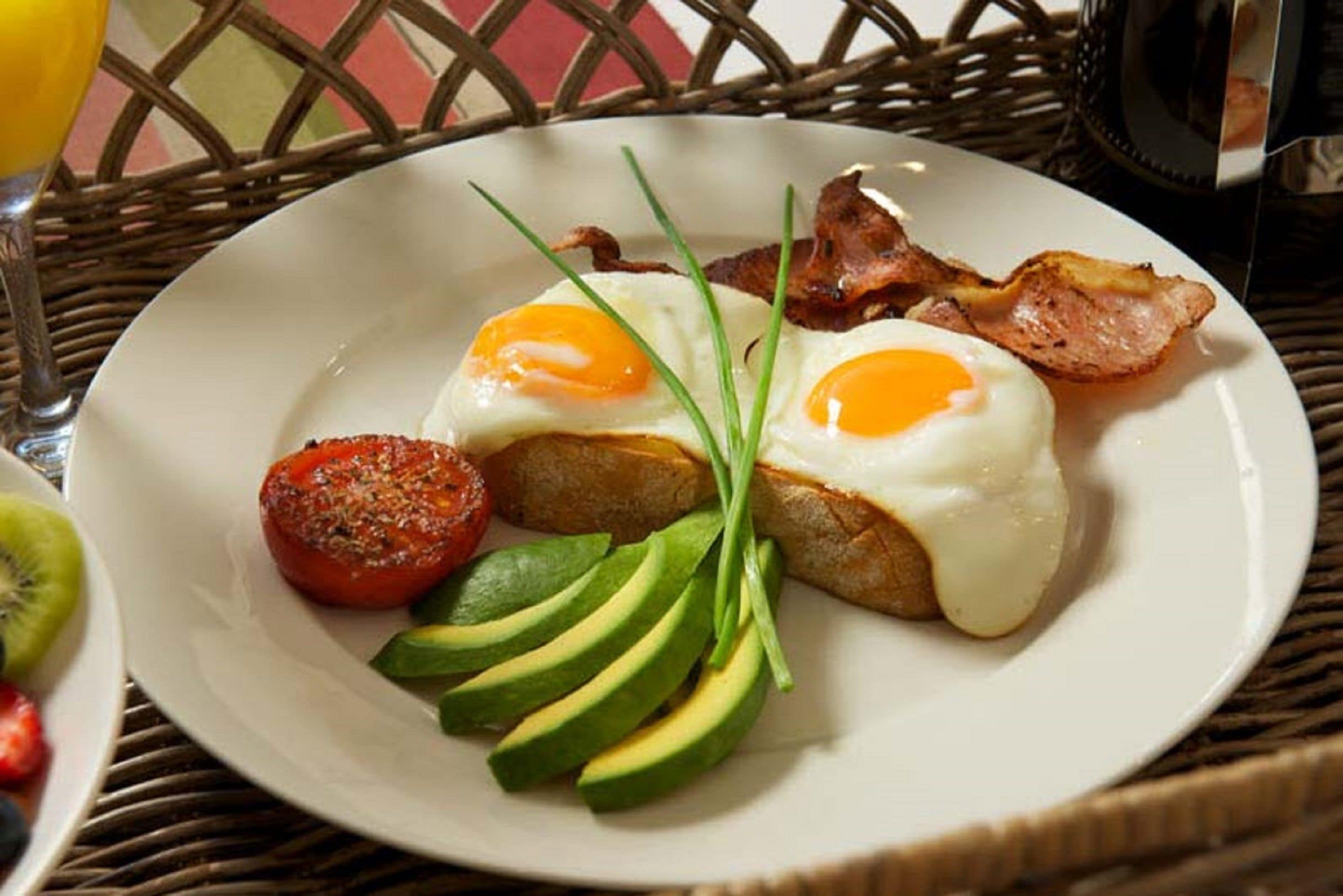 Un plato de desayuno con huevos, tocino, aguacate, tomate y cebollín.