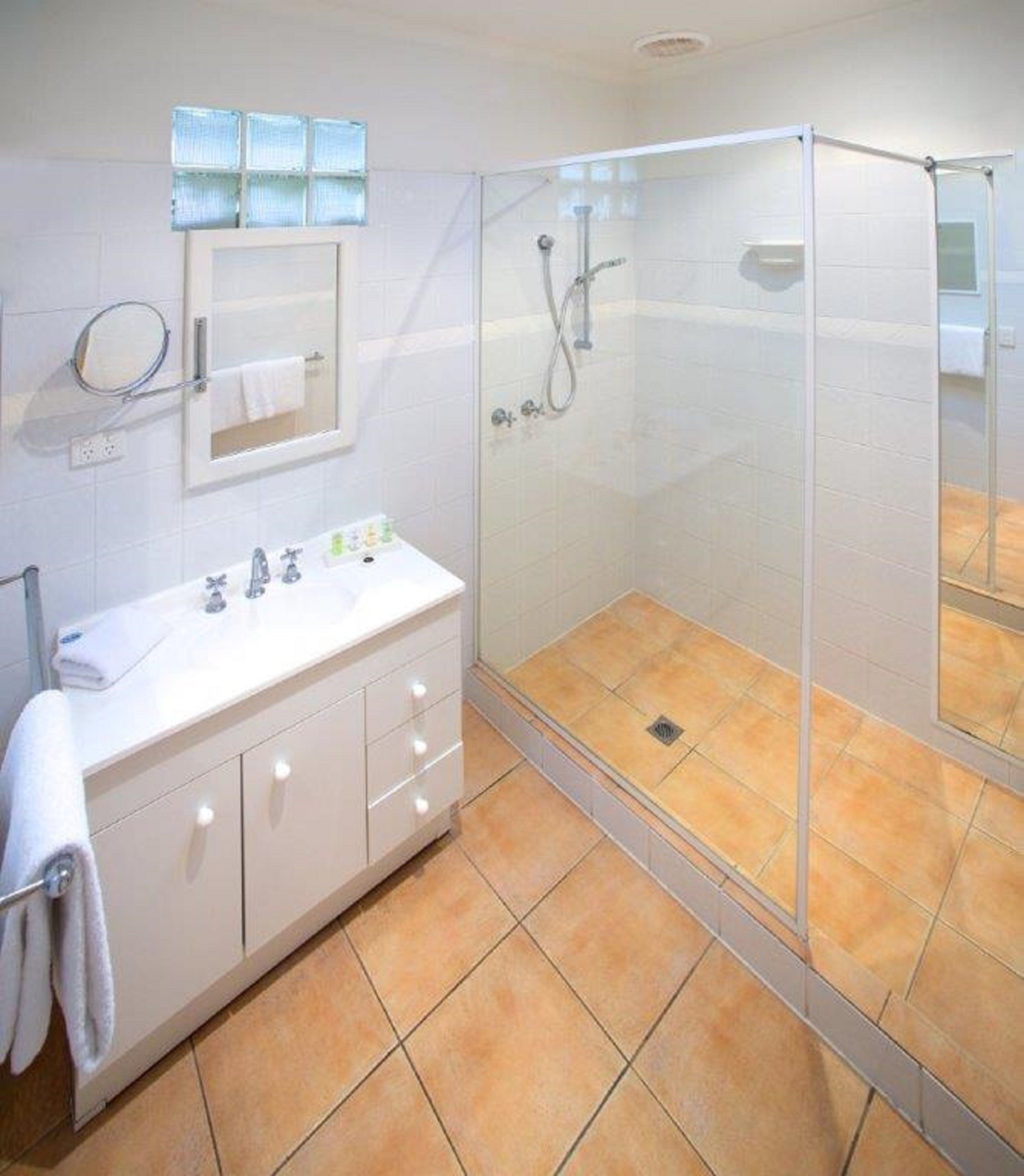 A bathroom with a glass-enclosed shower, a white vanity with a mirror, and a tiled floor.