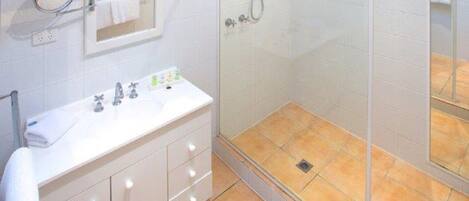 A bathroom with a glass-enclosed shower, a white vanity with a mirror, and a tiled floor.
