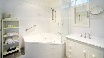 A modern bathroom with a glass-enclosed shower, a large bathtub, a vanity with a mirror, and shelves with towels.