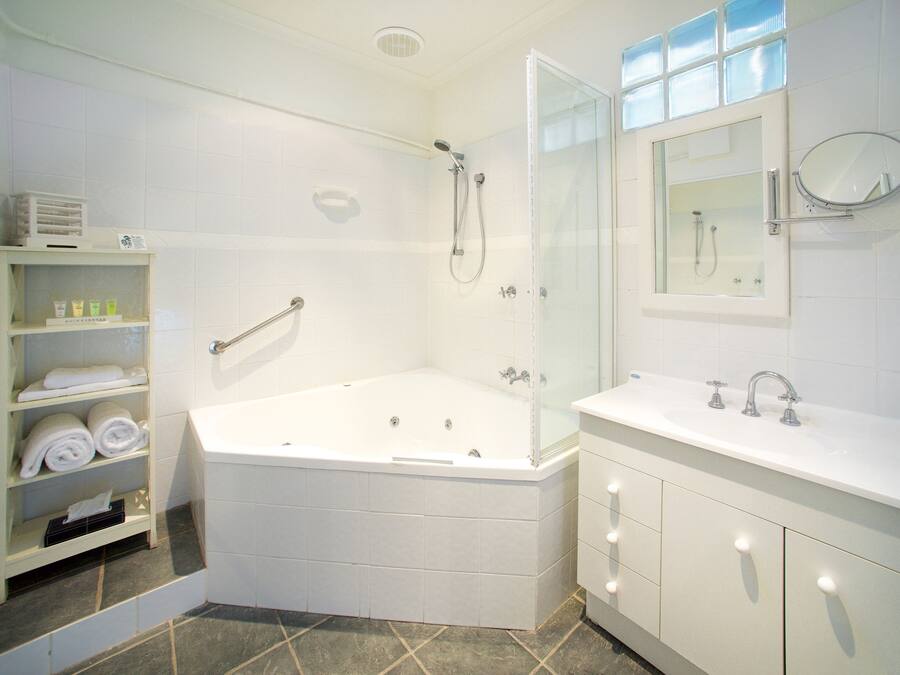 A modern bathroom with a glass-enclosed shower, a large bathtub, a vanity with a mirror, and shelves with towels.