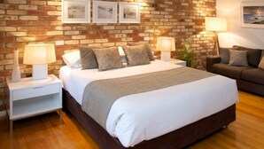 A bedroom with a brick wall, a bed with a white duvet, a grey sofa, and two bedside tables with lamps.