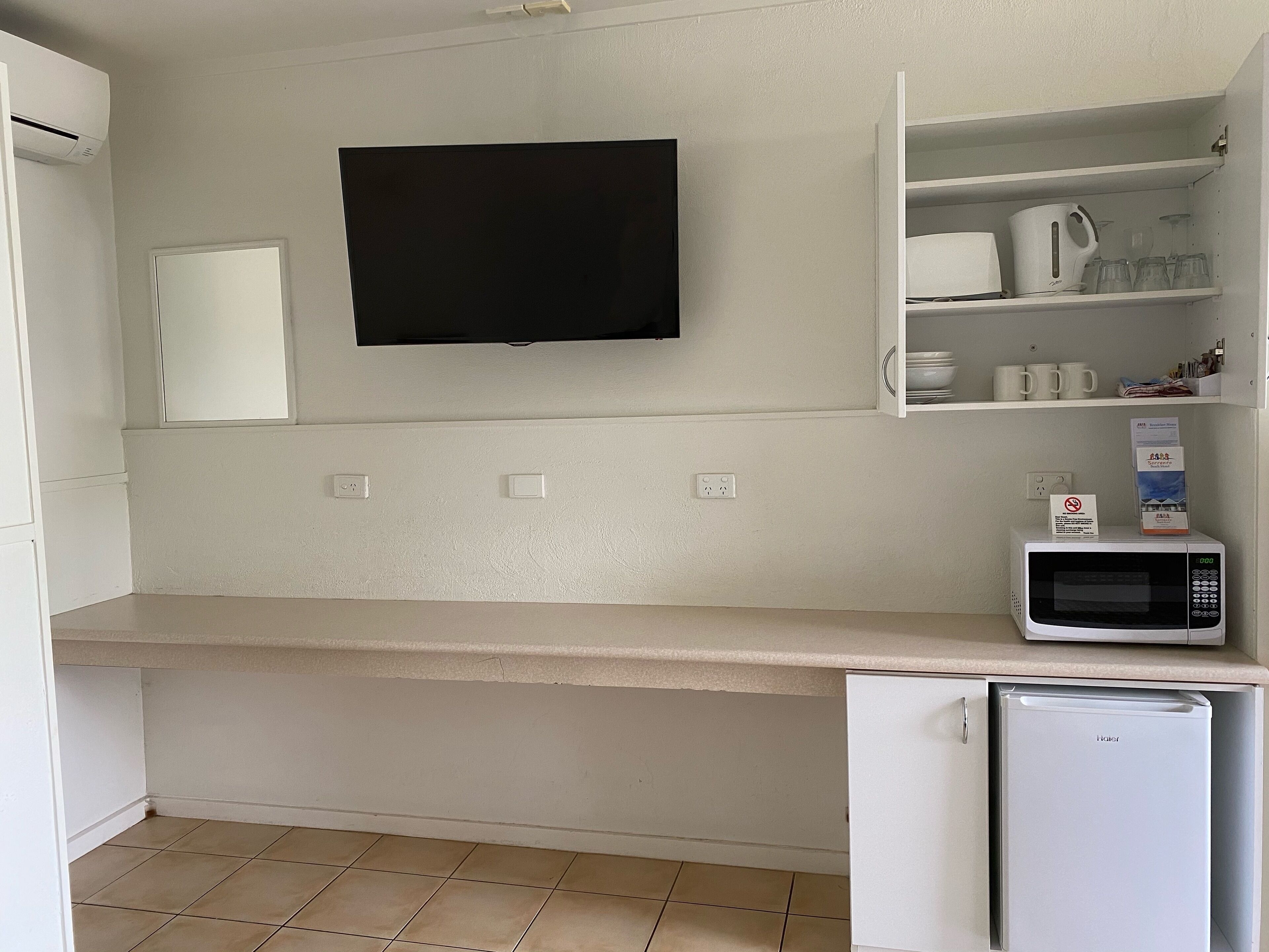 A kitchen with a flat-screen TV mounted above a countertop, a microwave, and a refrigerator.