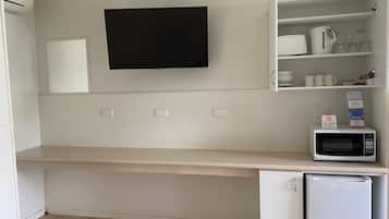 A kitchen with a flat-screen TV mounted above a countertop, a microwave, and a refrigerator.