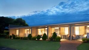 A modern hotel with a covered outdoor seating area, a well-maintained lawn, and a clear sky.
