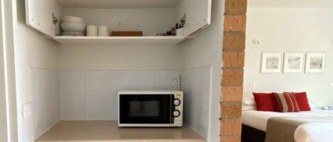 A compact kitchenette with a microwave, storage cabinets, and a trash bin.