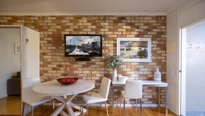 A dining area with a brick wall, a TV mounted above a table, and a window to the right.