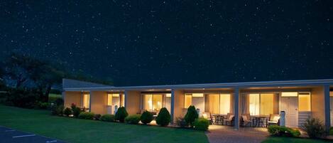 Un motel con un área de estar cubierta al aire libre, un césped bien cuidado y un cielo nocturno estrellado.